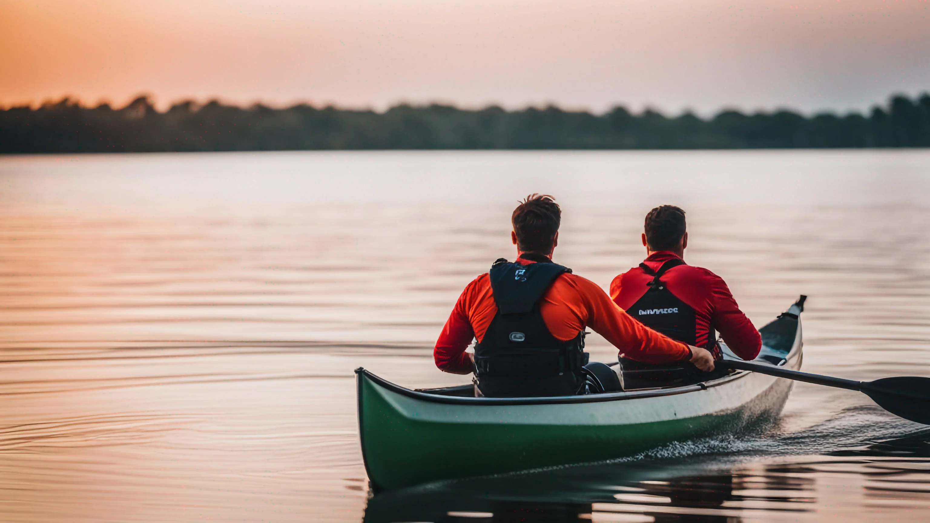 Two paddlers in a Green Voyage tandem canoe on a calm lake at sunset